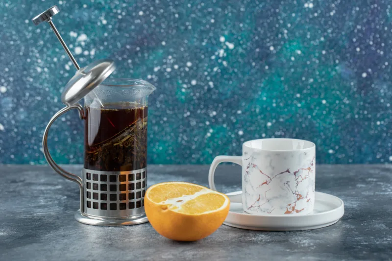 Teapot with cup of tea and fresh lemon over grey background