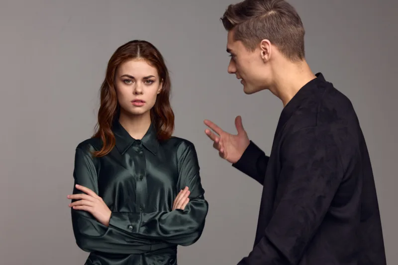 An indignant man in a black jacket gestures with his hands and looks at the woman