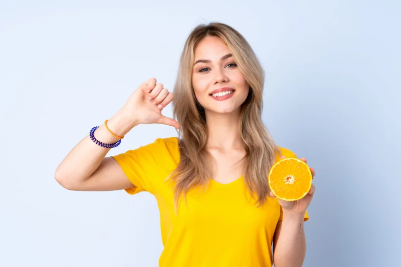 Teenager Russian girl holding an orange isolated on blue background proud and self-satisfied