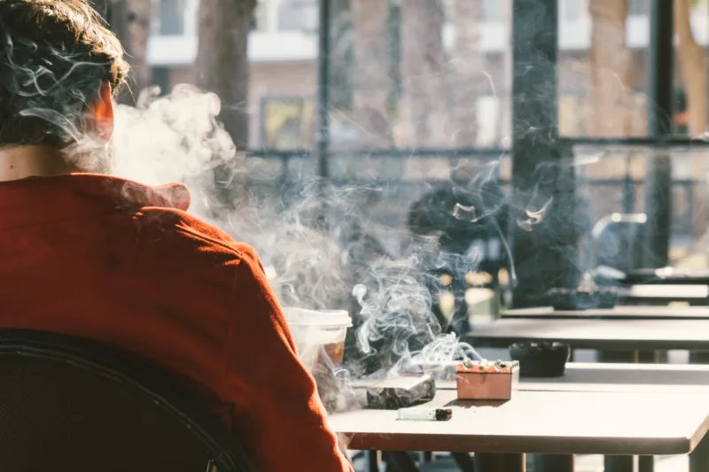 Back view of man smoking tobacco cigarette in cafe. Unhealthy lifestyle.