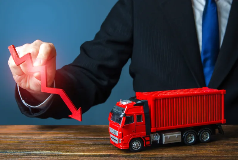 A businessman holds a red arrow down and a truck. Low sales. Production decline. Import, export. End of global containers shortage crisis. Transportation inflation, shipping rates. Priced drop
