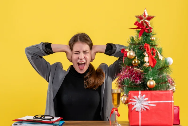 front-view-shouted-girl-sitting-desk-covering-ears-with-her-hands-xmas-tree-gifts-cocktail