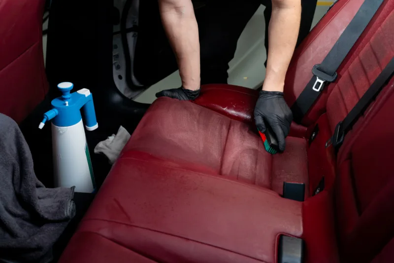 Cleaning car seats with detailing brush and bottle of soap liquid. Hand brushes car backseats with cleaning solution.