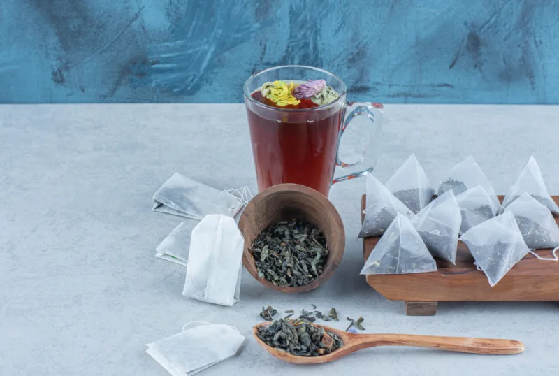 Overturned bowl full of tea leaves ,spoon,a cup of tea and tea bags on the board, on the marble background