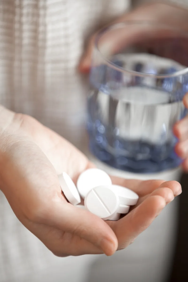 Handful of white round pills and glass of water in womans hands