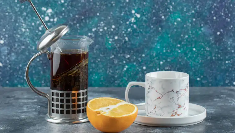 Teapot with cup of tea and fresh lemon over grey background