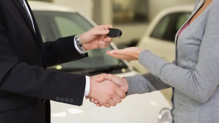 Businessman giving car key while shaking a customer hand at new car showroom