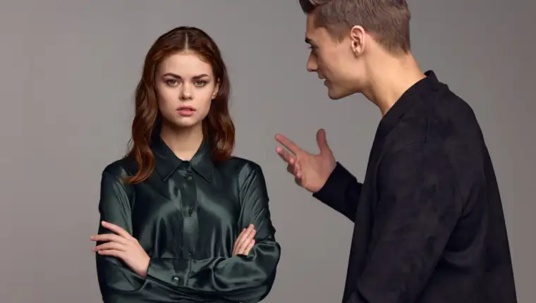 An indignant man in a black jacket gestures with his hands and looks at the woman