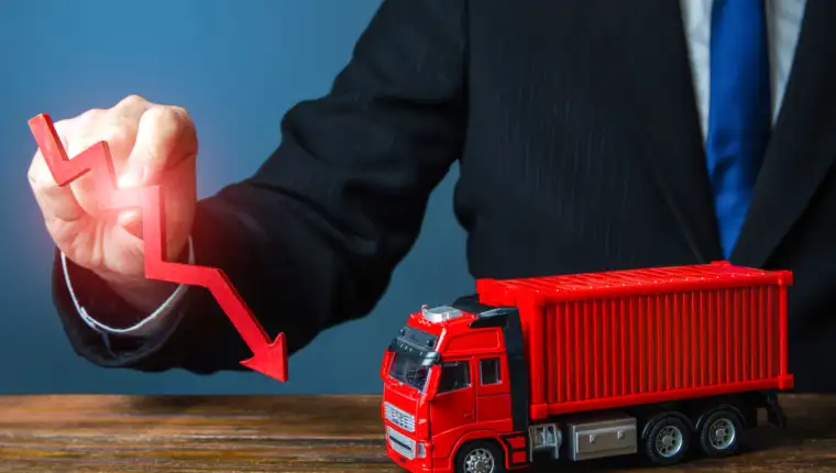 A businessman holds a red arrow down and a truck. Low sales. Production decline. Import, export. End of global containers shortage crisis. Transportation inflation, shipping rates. Priced drop
