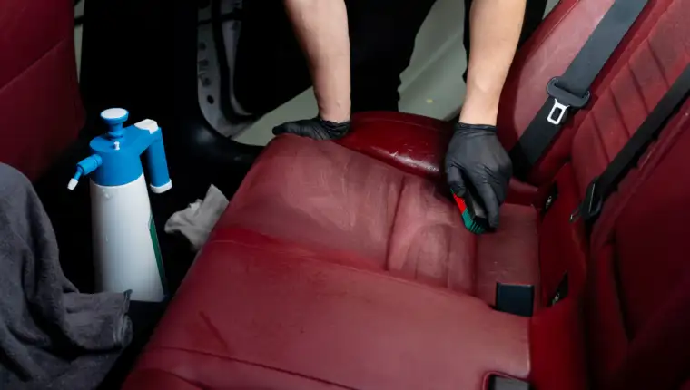 Cleaning car seats with detailing brush and bottle of soap liquid. Hand brushes car backseats with cleaning solution.