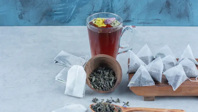 Overturned bowl full of tea leaves ,spoon,a cup of tea and tea bags on the board, on the marble background