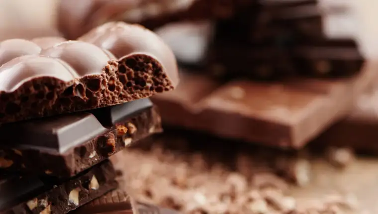Composition of bars and pieces of different milk and dark chocolate, grated cocoa on a brown background side view close up