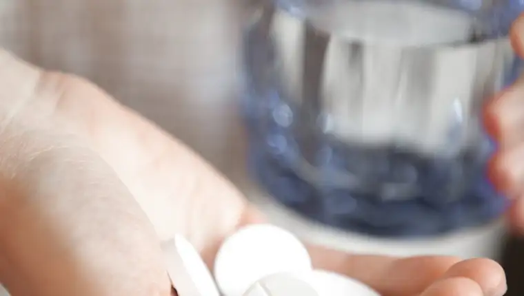 Handful of white round pills and glass of water in womans hands