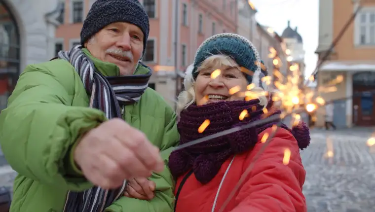 Senior happy couple with burning sparklers bengal lights celebrating birthday on city center street