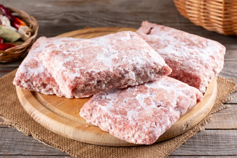 Frozen ground meat, minced pork on a wooden board. Ground chicken inclusive backs, necks, liver and heart. Frozen food. Concept for raw food diet for cats, dogs and pets.