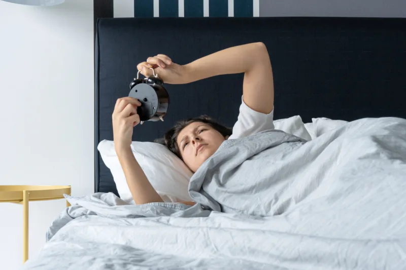 The girl turns off the annoying alarm clock to continue sleeping. Get some more sleep. It a hard morning. Time to wake up.