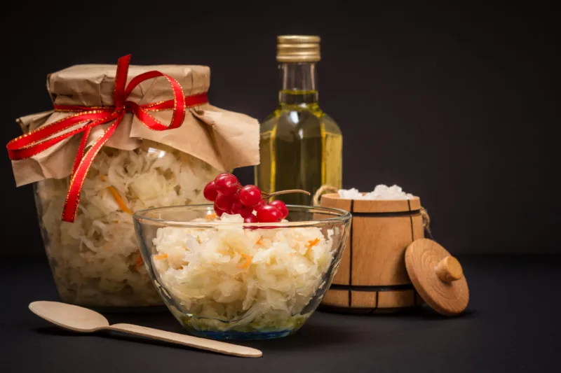 Fermented cabbage with herbs and spices in glass bowl and jar on the black background