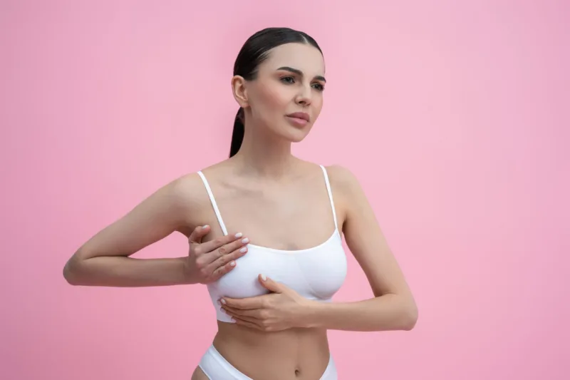 Young woman in white bra examining her breast with her hand