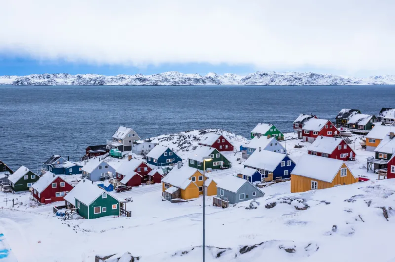 Colorful inuit houses among rocks and snow at the fjord in a sub