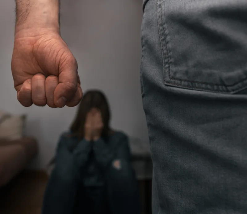 Man raises his fist to mistreat a helpless woman, sitting on the ground, covering her face with her hands, frightened