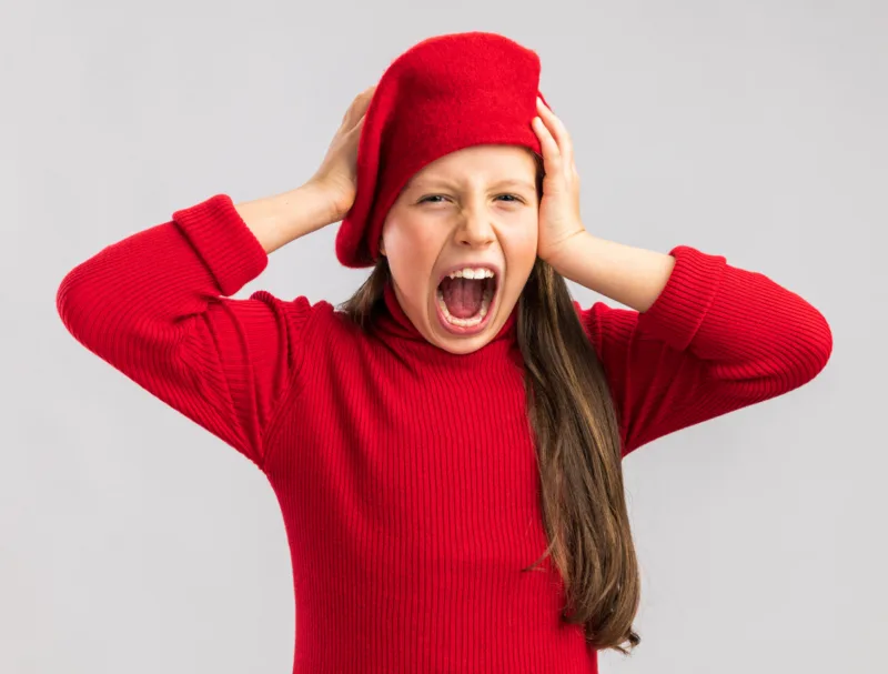 stressed little blonde girl wearing red beret keeping hands on head looking at camera and screaming isolated on white background