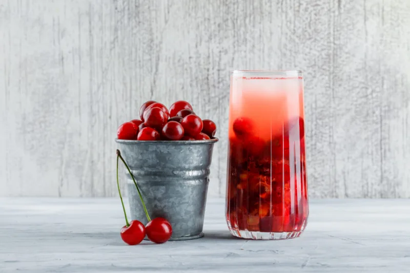 Cherry cocktail in a jug with cherries side view on a grungy background