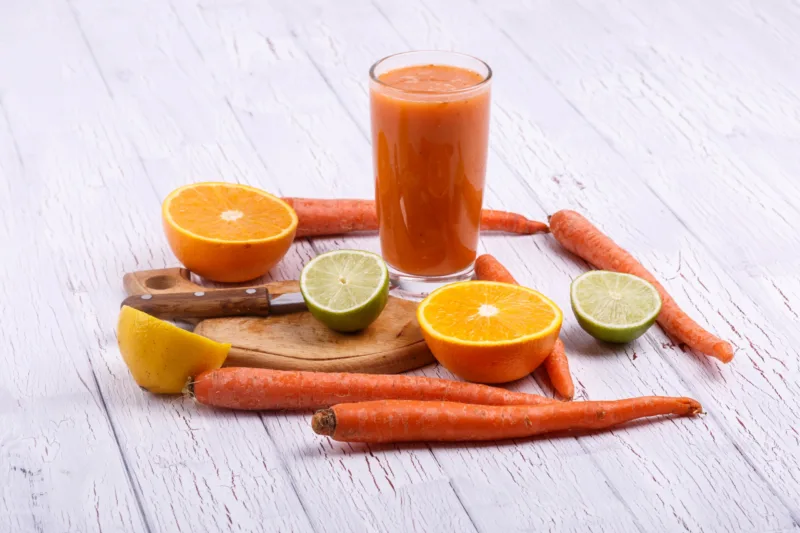 orange detox coctail with oranges,lime and carrots lies on white