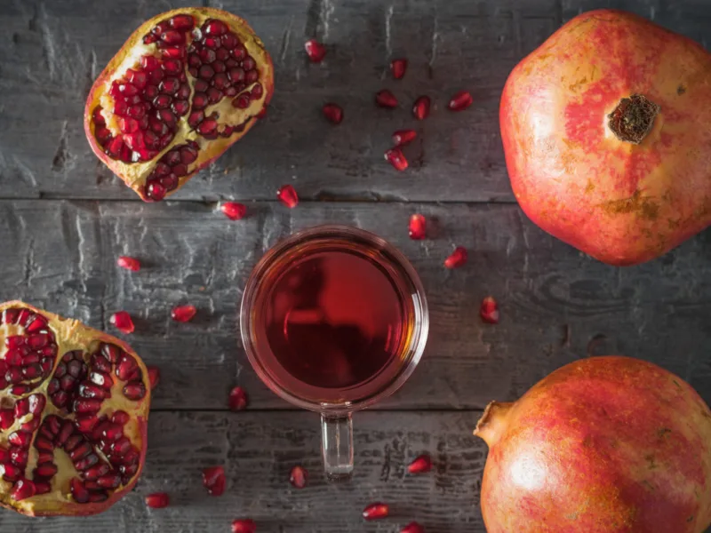 Glass mug with pomegranate juice and fresh pomegranates on a wooden table. Flat lay.