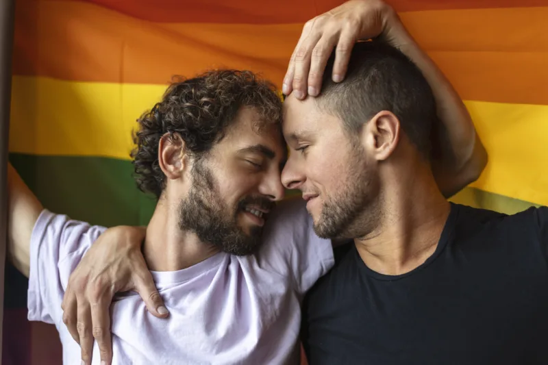 Passionate gay couple making out with lgbtq flag in the background. Young gay couple bonding fondly indoors.