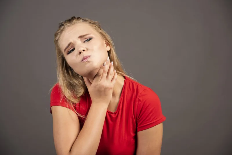 Young woman holding her throat on dark background