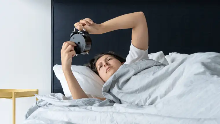 The girl turns off the annoying alarm clock to continue sleeping. Get some more sleep. It a hard morning. Time to wake up.