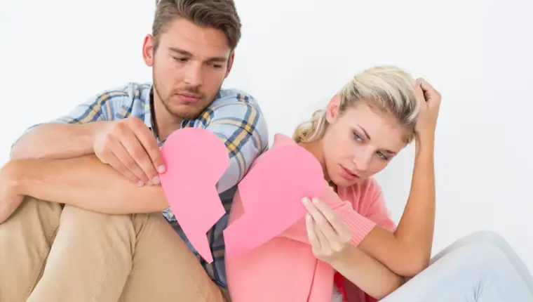 Young couple holding two halves of broken heart over white background