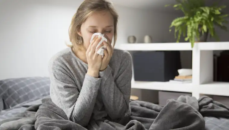 Sick woman sitting in bed, blowing nose with napkin