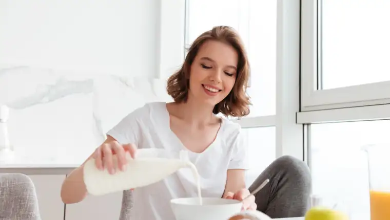 Portrait of a smiling young woman pouring milk