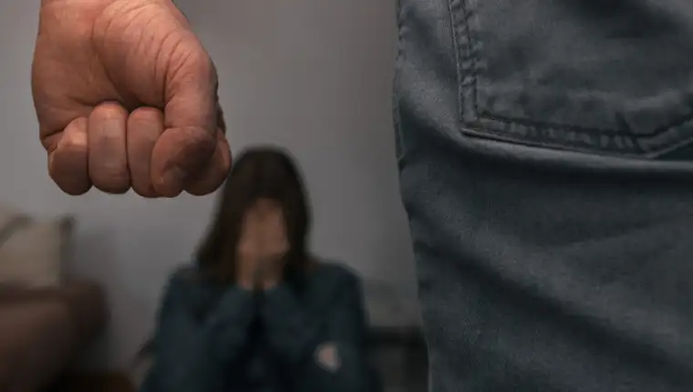 Man raises his fist to mistreat a helpless woman, sitting on the ground, covering her face with her hands, frightened