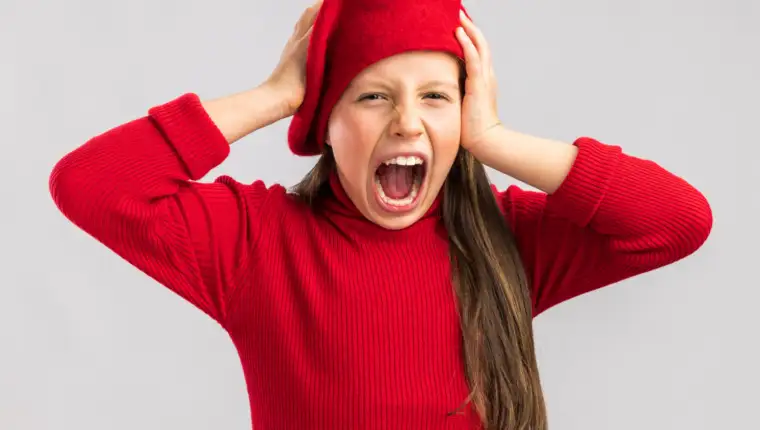 stressed little blonde girl wearing red beret keeping hands on head looking at camera and screaming isolated on white background
