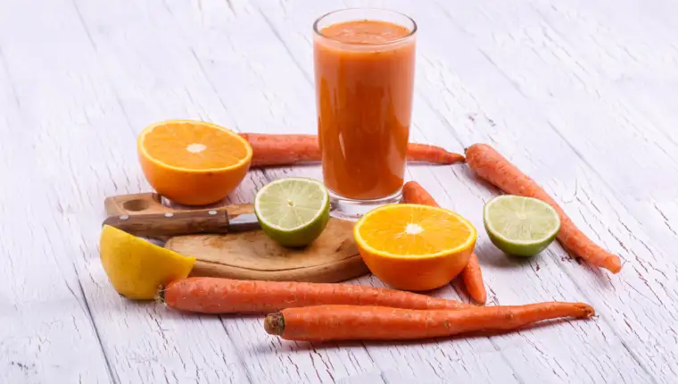 orange detox coctail with oranges,lime and carrots lies on white