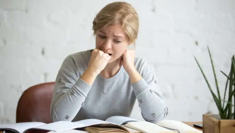 Portrait of a student girl sitting at the desk biting her fist