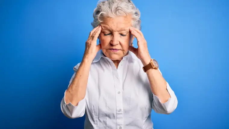 Senior beautiful woman wearing elegant shirt standing over isolated blue background with hand on head for pain in head because stress. Suffering migraine.