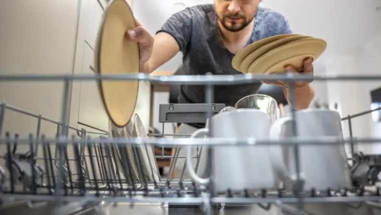 The man takes the washed dishes from the dishwasher.