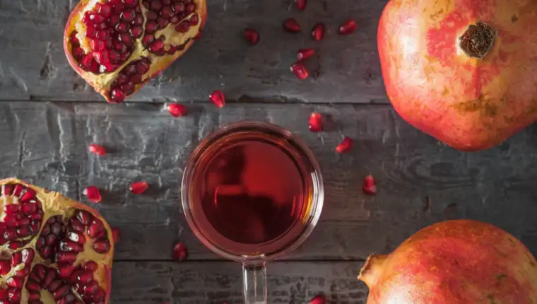Glass mug with pomegranate juice and fresh pomegranates on a wooden table. Flat lay.