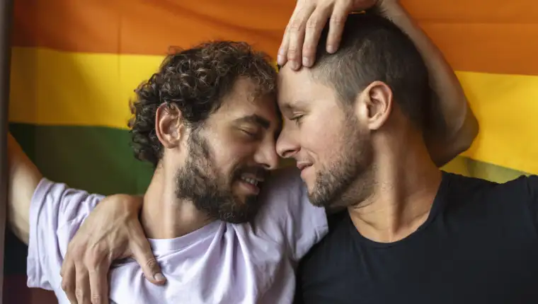 Passionate gay couple making out with lgbtq flag in the background. Young gay couple bonding fondly indoors.