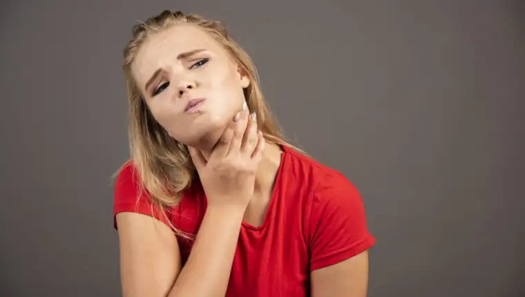 Young woman holding her throat on dark background