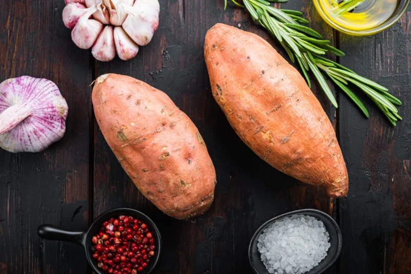 Sweet potato or batat with herbs on old wooden table, top view