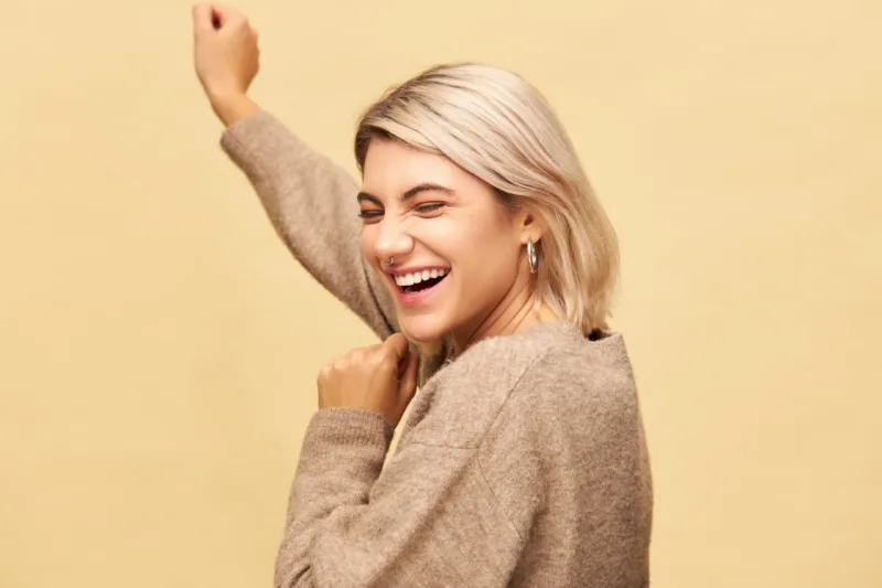 Positive human emotions and feelings. Joyful happy young woman with bob hairstyle and nose ring celebrating success, laughing and dancing, having cheerful facial expression, posing isolated in studio