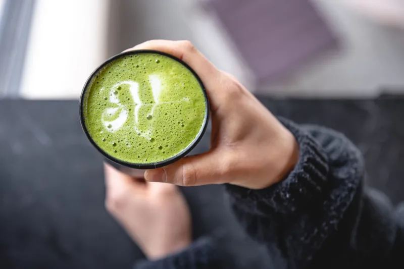 Cup of Matcha Green Tea in woman hand, top view.
