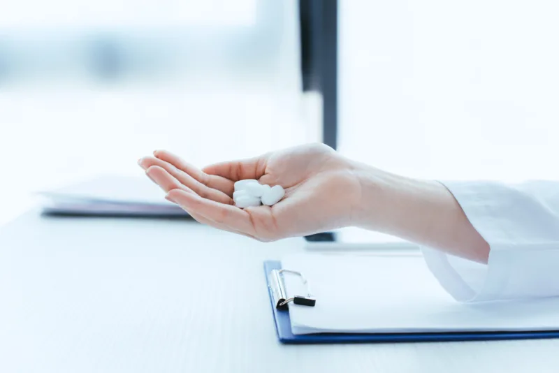 cropped shot of doctor with handful of pills near clipboard on table