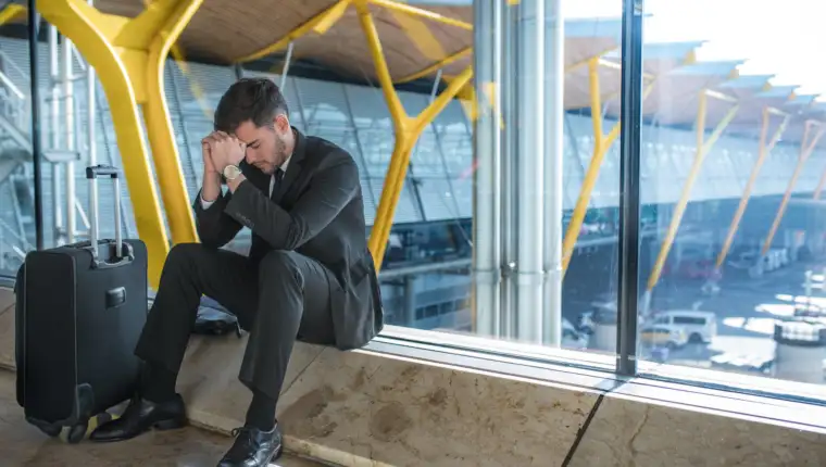 young businessman upset at the airport waiting his delayed flight with luggage