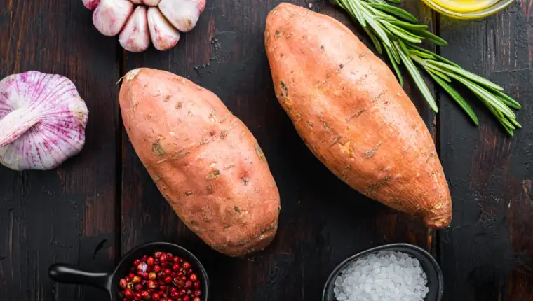 Sweet potato or batat with herbs on old wooden table, top view