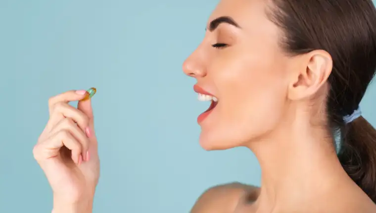 Close-up beauty portrait of a topless woman with perfect skin and natural make-up, holding a supplement, vitamin omega 3, fish oil, on a turquoise background